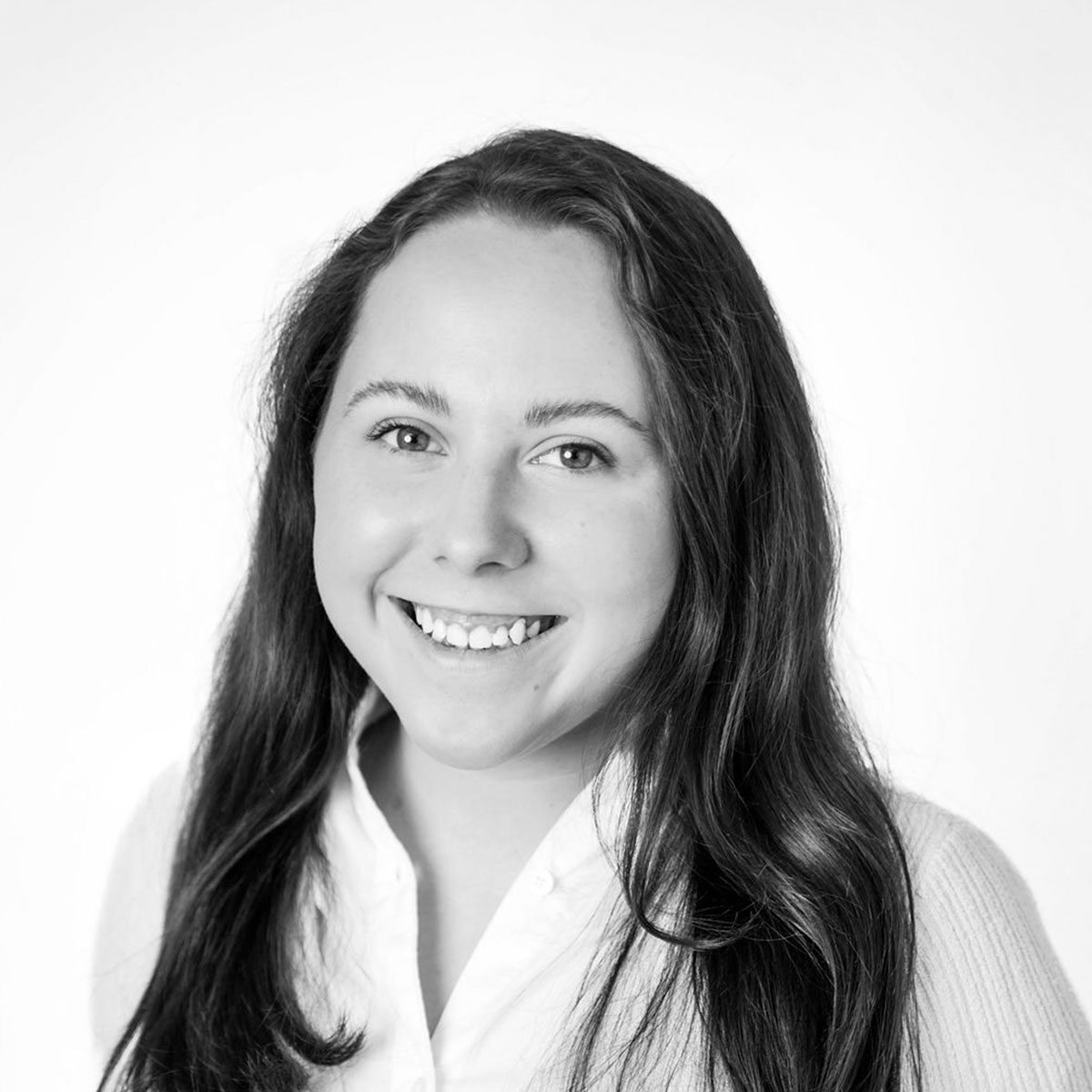 resized-kaitlynn-jenkins Black and white portrait of Kaitlynn Jenkins with long dark hair, smiling, wearing a white shirt and light-colored sweater, against a plain background.